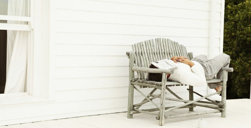 Man sleeping on a bench on the porch outside his home , newspaper on face